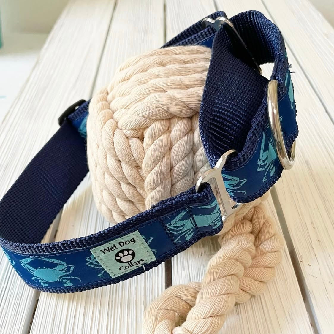 Navy blue dog collar with crab pattern and beige rope ball on a light wooden surface