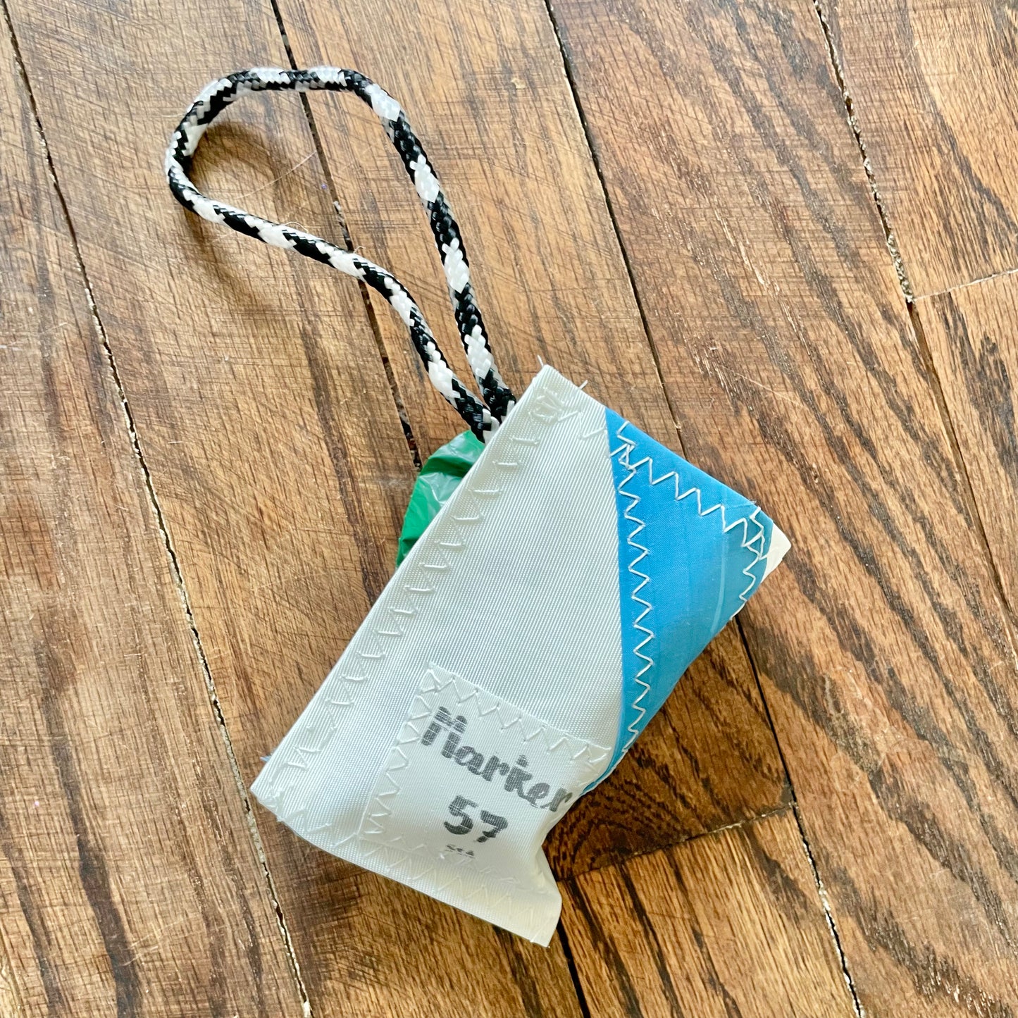 Small fabric pouch with a blue corner and black and white rope handle on a wooden surface