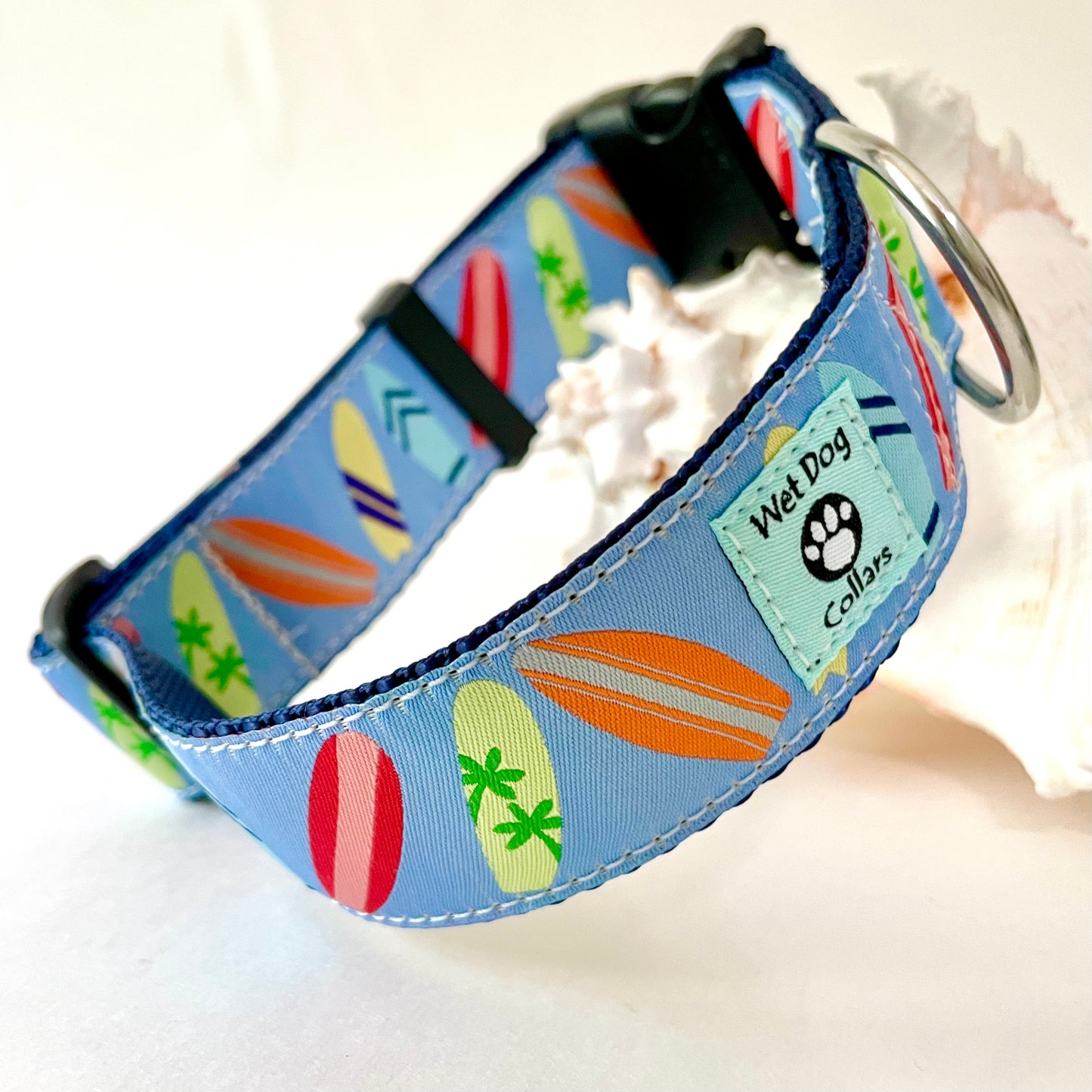 A blue fabric dog collar with a colorful surfboard pattern, featuring a rust proof D-ring