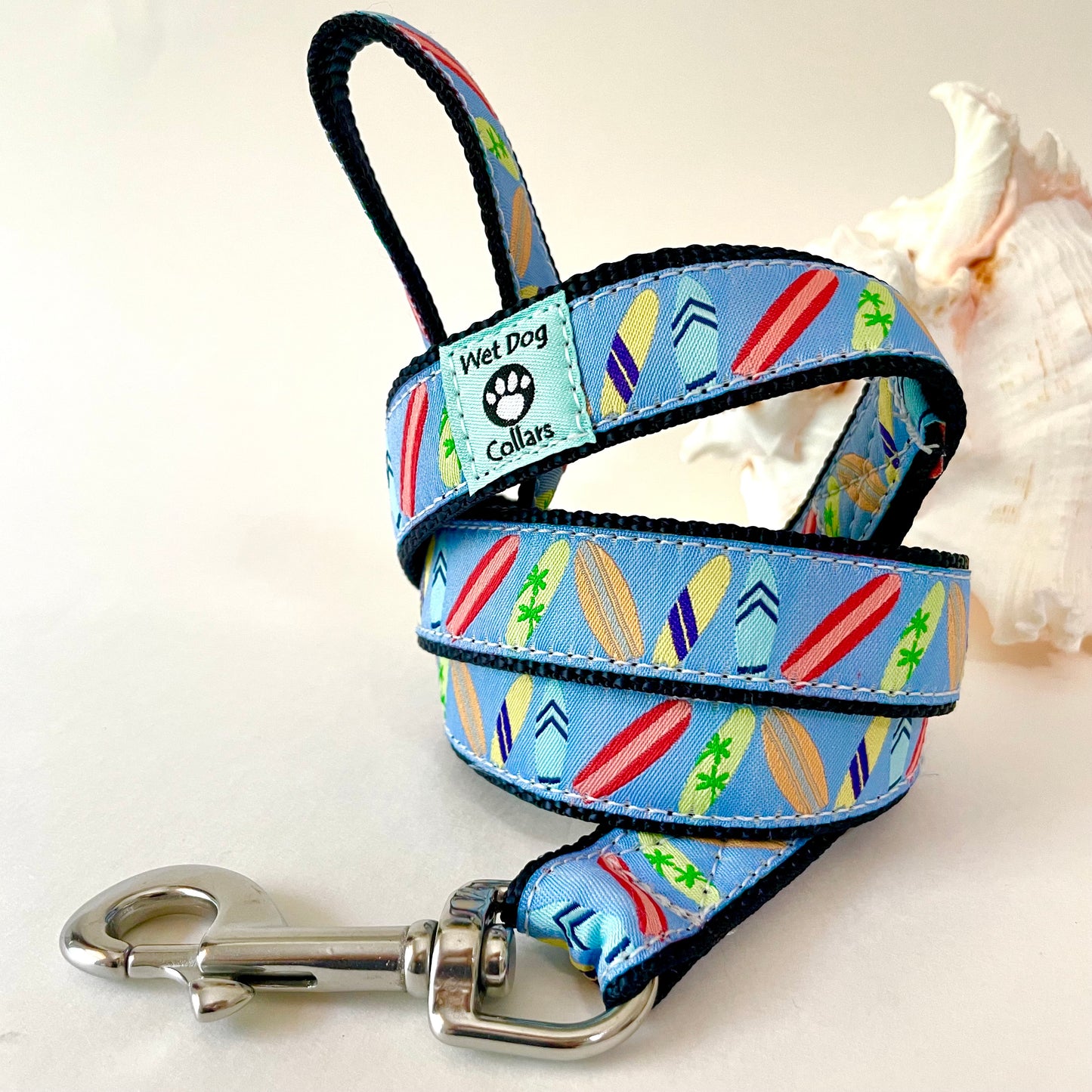 A coiled blue dog collar with a colorful surfboard pattern and a rust proof clip